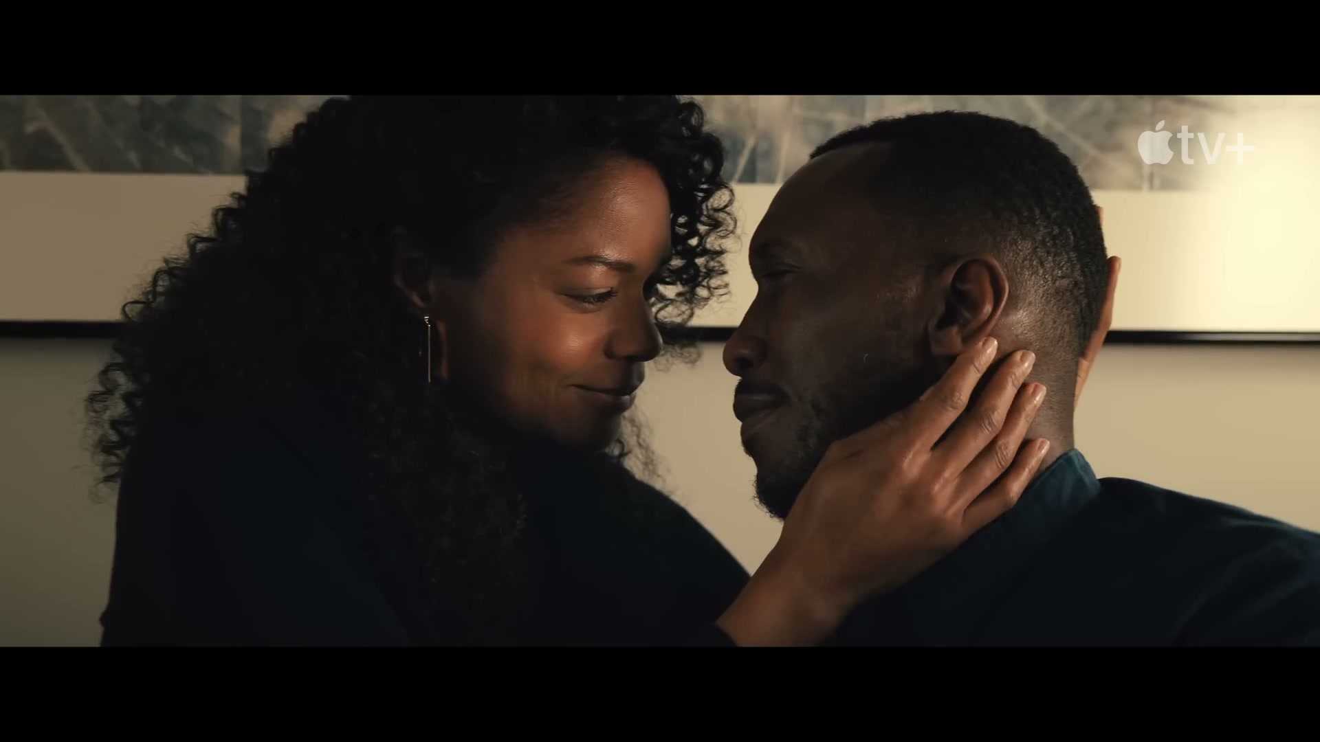 Frame from the official Swan Song trailer at 0:23 — Mahershala Ali and Naomie Harris face-to-face. Hayashi's Bodhi Tree panorama spans the wall behind them. Apple TV+ chose this as the YouTube thumbnail.